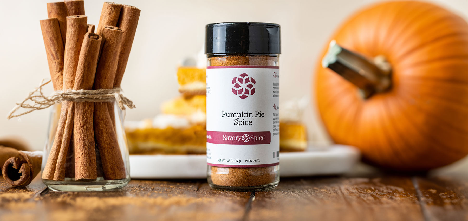 A bundle of cinnamon sticks, a jar of Pumpkin Pie Spice, a pumpkin (left to right)