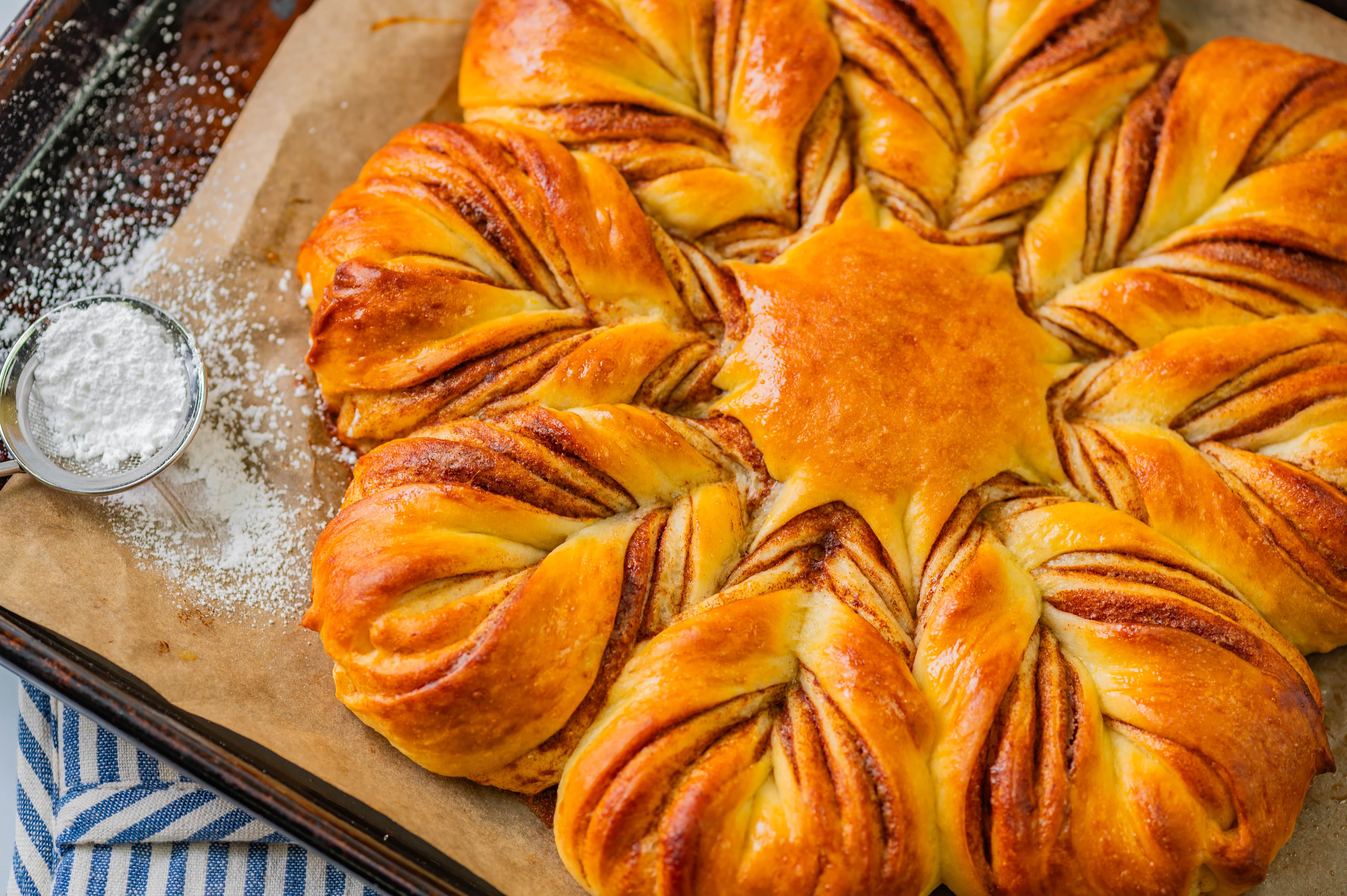 Baked, twisted Star Bread on a pan with a sifter of powdered sugar next to it