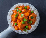 Overhead of a white bowl of Tikka Masala over rice served with peas and carrots on a black background