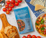 Overhead shot of a packet of Sun-Dried Tomato Minestrone Spice & Easy mix on a table with bread, cheese, tomatoes, and a finished bowl of soup