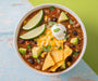 Overhead bowl of  Taco Soup garnished with avocado, lime, cheese, sour cream, and tortilla chips