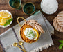 Overhead of a table set with a gold bowl of Moroccan Lentils garnished with flatbread, sour cream, lemon and herbs