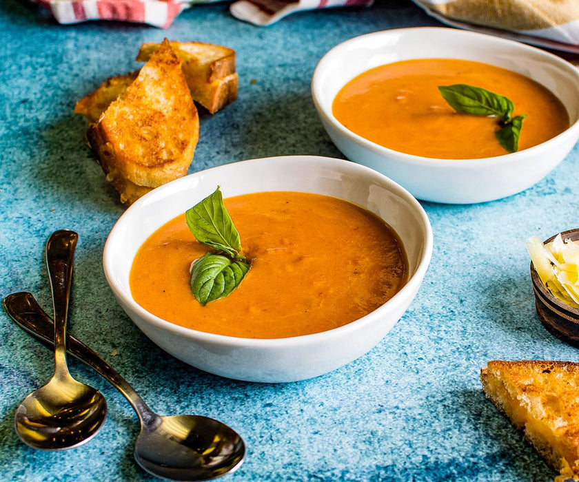 two finished white bowls of Toasty Tomato Bisque soup with grilled cheese